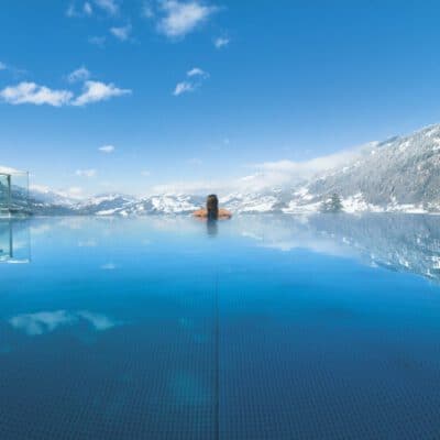 Alpinas Rooftop Pool mit Ausblick auf verschneite Berge im Winter