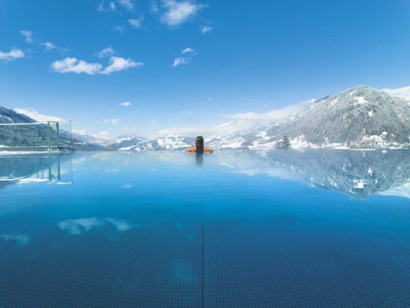 Alpinas Rooftop Pool mit Ausblick auf verschneite Berge im Winter
